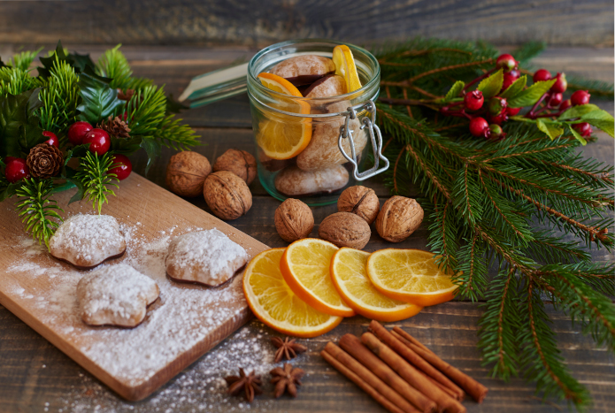 pierniczki posypane cukrem pudrem w świątecznej aranżacji z pomarańczami i orzechami